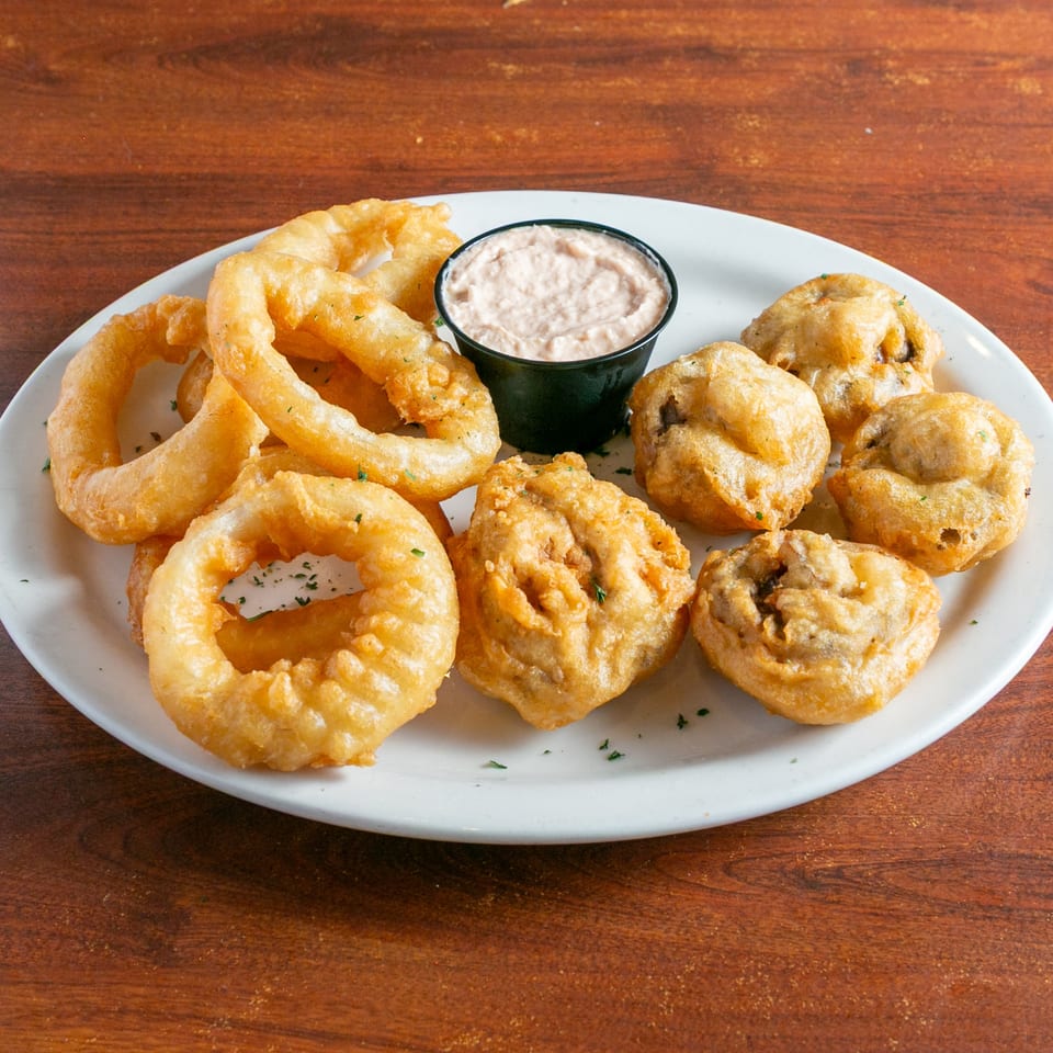 Plate of golden fried onion rings and battered vegetables served with creamy dipping sauce on a wooden table.