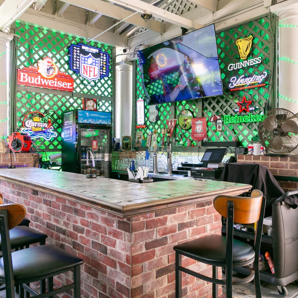 Brick-front sports bar with tiled counter, televisions, beer taps, and colorful Budweiser, Guinness, Heineken, and Corona signs.