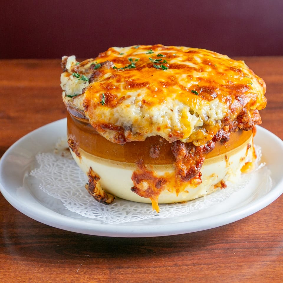 Loaded cheeseburger topped with melted cheddar, crispy bacon, and parsley on a white plate.