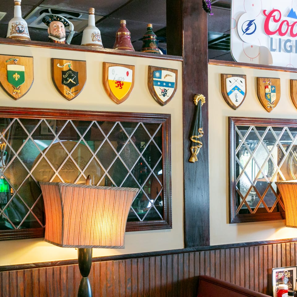 Traditional pub interior with heraldic shields, decorative ceramic bottles, Coors Light sign, mirrored windows, and warm lamps.