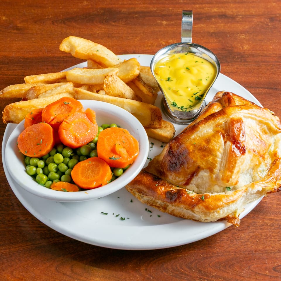 Golden pot pie served with thick-cut fries, peas and carrots, and a small dish of creamy yellow sauce.