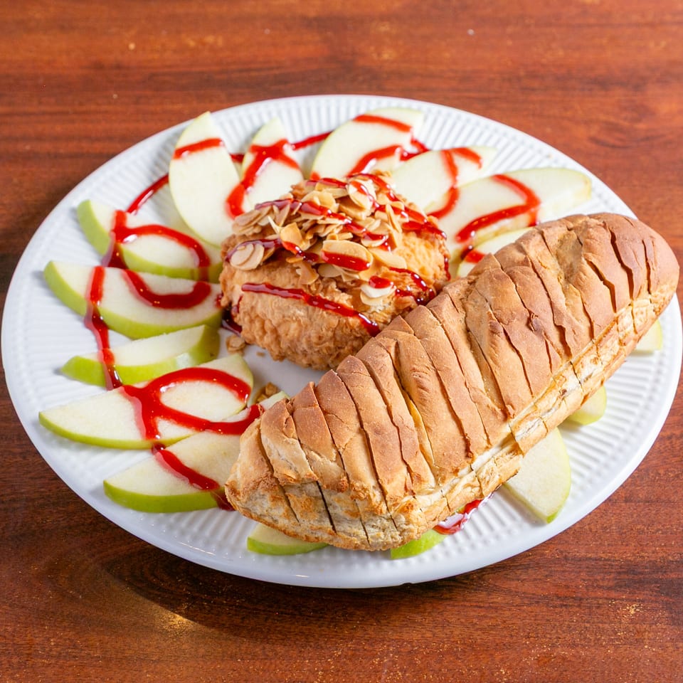 Sliced bread, an almond-topped pastry, and green apple wedges drizzled with red syrup sit on a white plate.